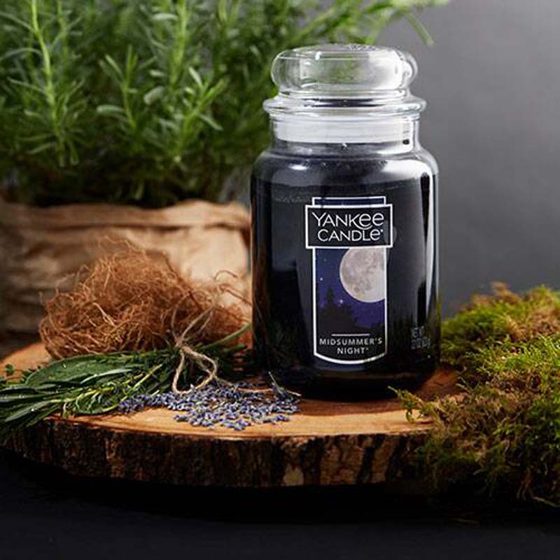 a black candle in glass with glass lid sitting on a slice of tree trunk and surrounded by moss and leaves