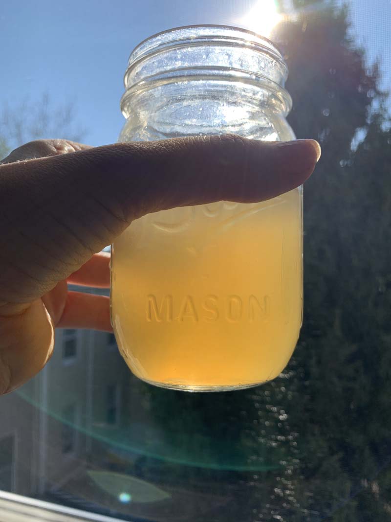 a mason jar full of syrup that's piss colored being held up