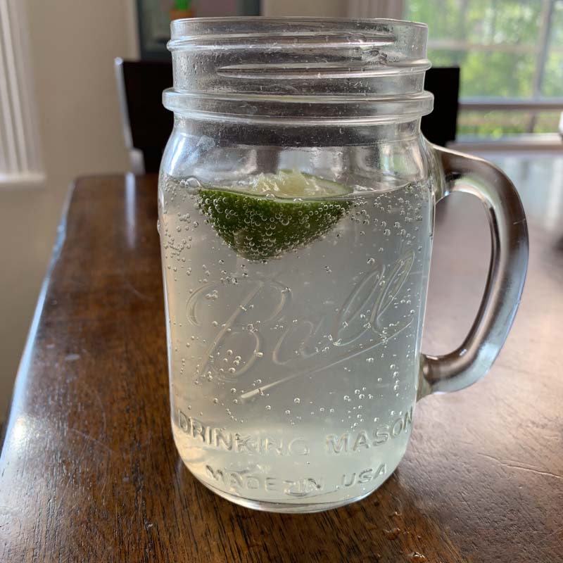 a mason jar with a fizzy drink and lime on a brown kitchen table