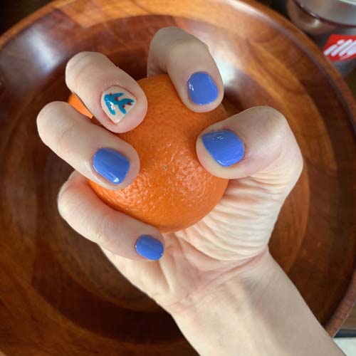 my right hand holding a mandarin showing off my nails, all the purplish neon solid color of the previous photo and with a single accent nail