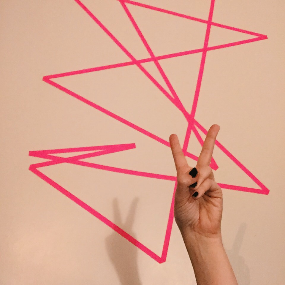 a photo of a hot pink line art on my bedroom wall and my hand giving the peace sign. i am in my bed but i lifted my webcam so you only see my hand and art.