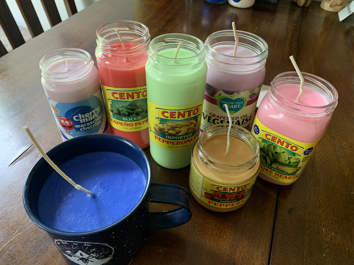 a photo of 7 candles i made with different pastel colors made of condiment jars and a tin mug