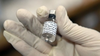 Health Care Worker holding a vial 
        of COVID-19 vaccine in gloved hand